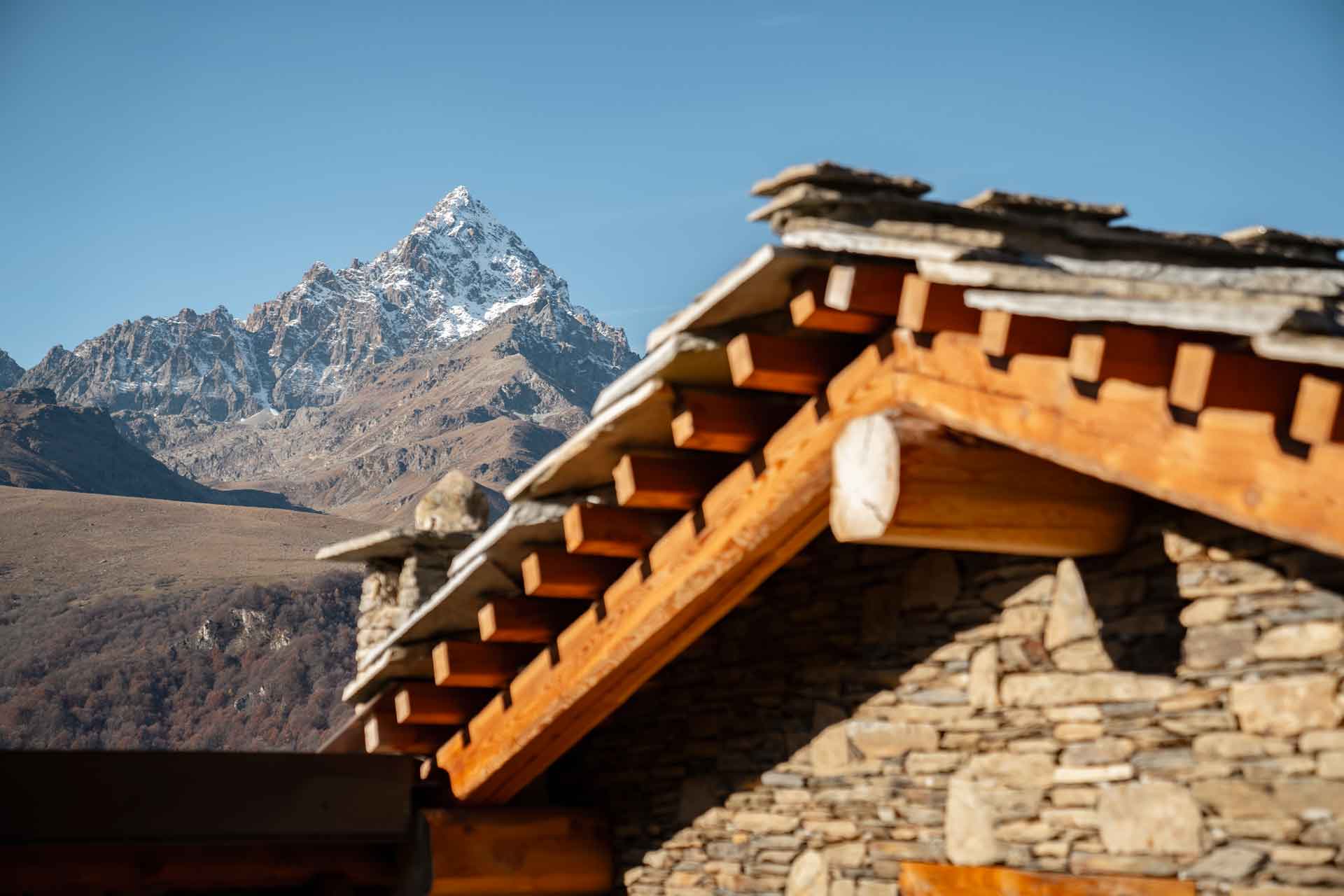 Dettaglio dei tetti in lose di pietra con travi in legno e il Monviso sullo sfondo