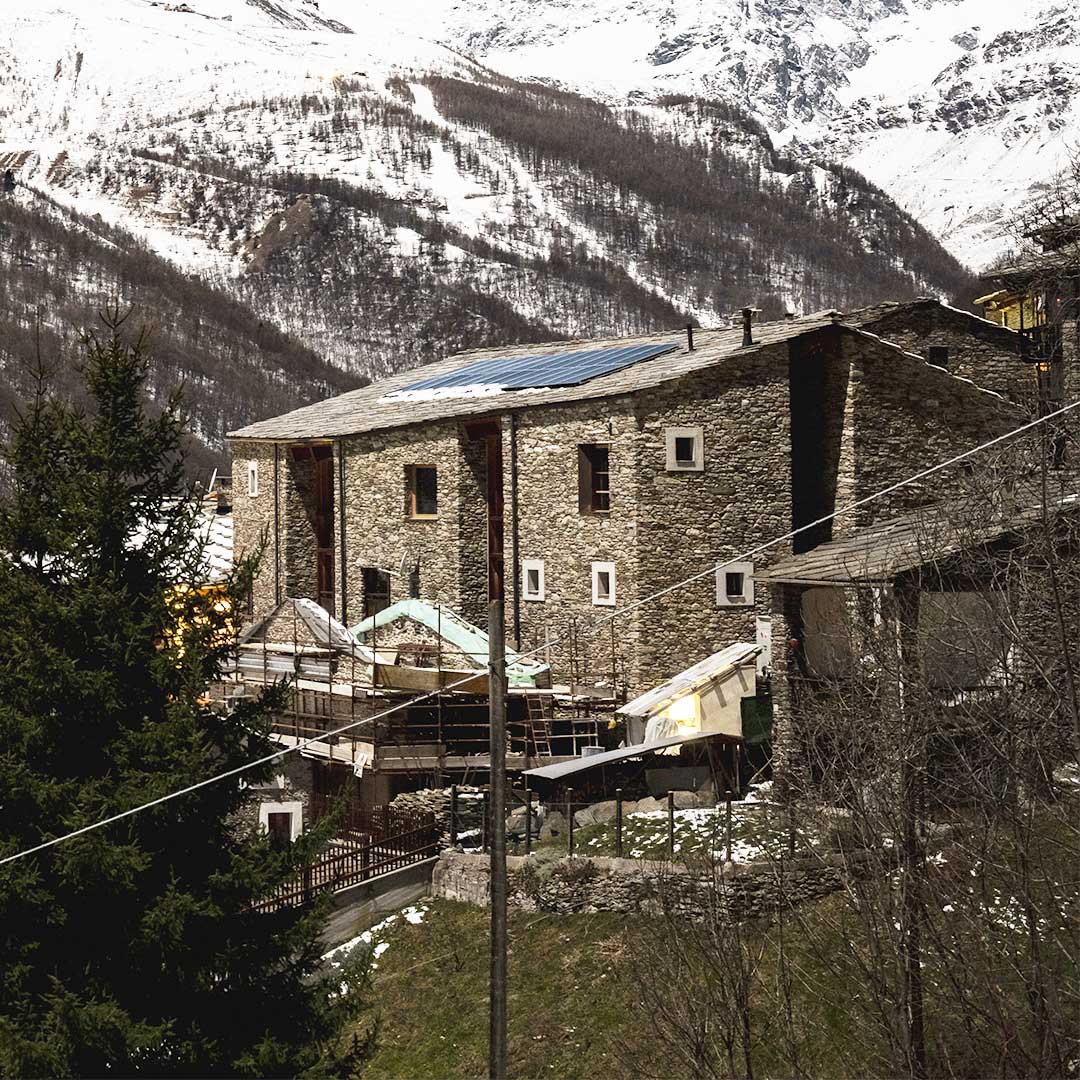 L'edificio Lou Pourtoun a Ostana, struttura in pietra con pannelli solari sul tetto e montagne innevate sullo sfondo